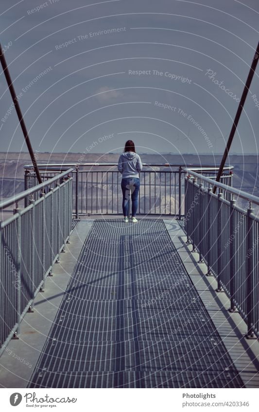 Junge Frau steht auf dem Skywalk am Aussichtspunkt Jackerath / Tagebau Garzweiler jung Haare grau Oberteil braun Sonne sonnig Erwachsene Mensch Außenaufnahme