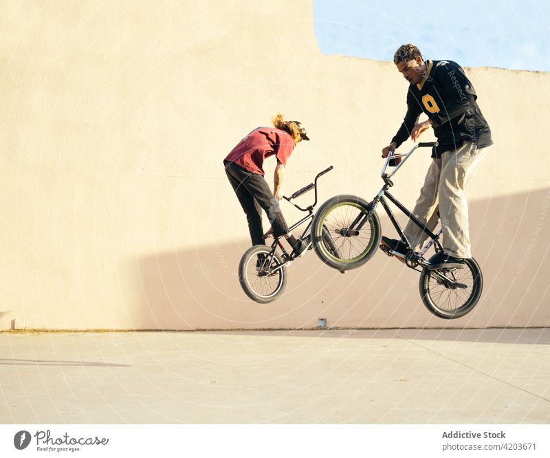 Multirassische Biker, die beim Training über dem Gehweg auf Trial-Bikes springen Fahrrad Testversion extrem Sport Freestyle Aktivität Männer Laufsteg Freund