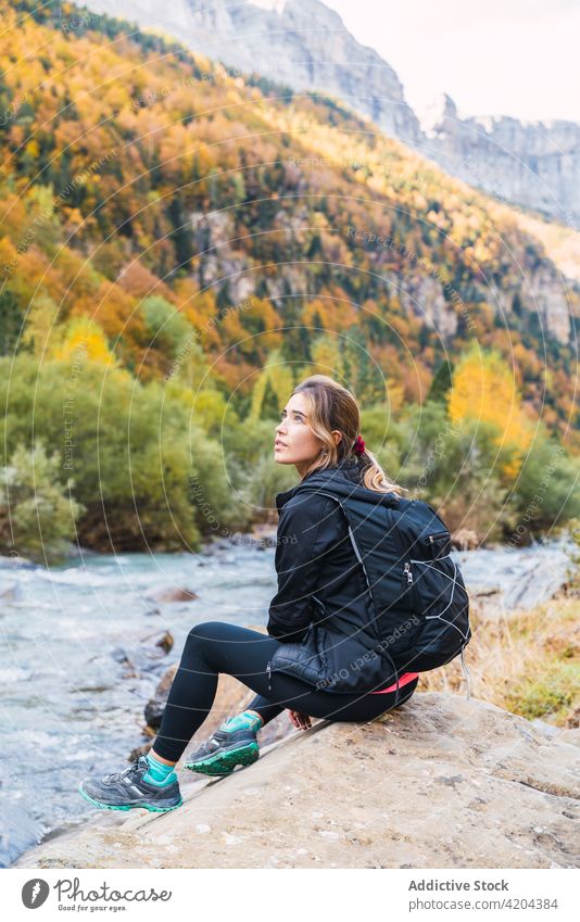 Reisender mit Rucksack sitzt auf Stein in der Nähe von Bergfluss Berge u. Gebirge Frau Fluss Hochland Wanderer Trekking reisen Felsen Pyrenäen Huesca Spanien