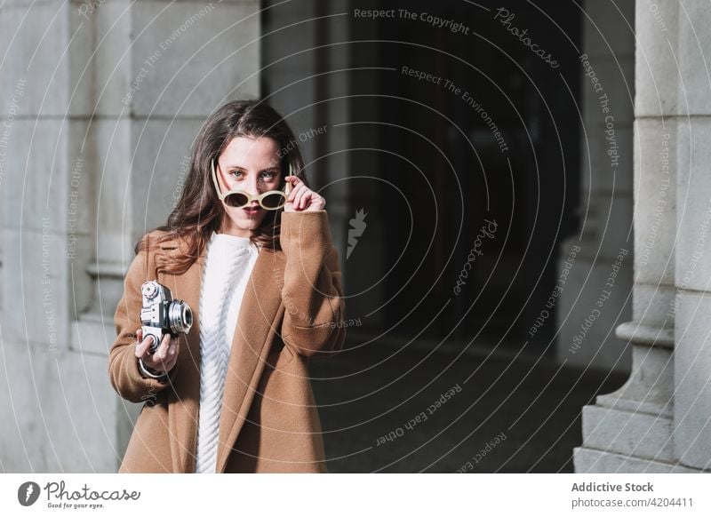 Trendige Frau mit Fotoapparat in der Stadt Stil Mantel altehrwürdig retro Großstadt trendy Nostalgie Sonnenbrille Fotokamera Straße Outfit Mode urban klassisch