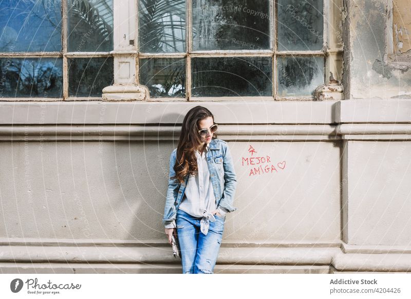 Stilvolle Frau steht in der Nähe von alten Gebäude in der Stadt Jeansstoff Jeanshose Outfit Großstadt urban schäbig trendy Sonnenbrille selbstbewusst Straße