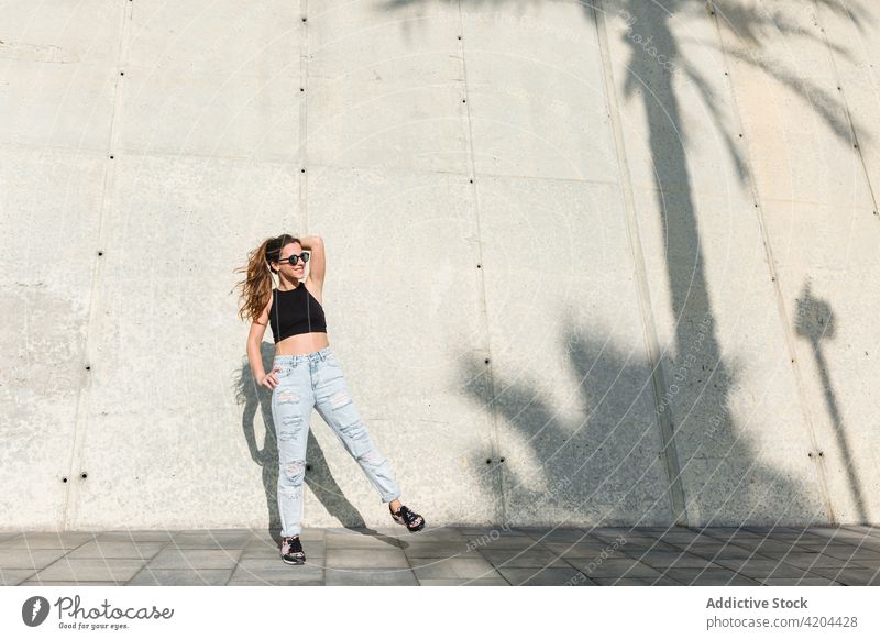 Junge Frau in trendigem Sommeroutfit Stil Outfit Sonnenbrille trendy Mode modern tropisch lässig jung Brille Accessoire Jeanshose Top Handfläche Lifestyle Dame