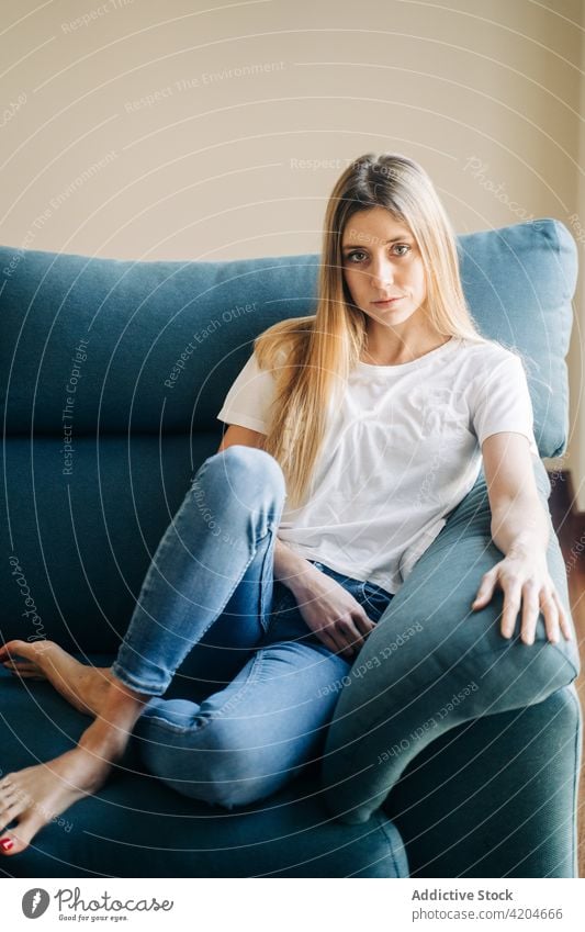 Ernste Frau auf Couch sitzend Liege Sofa Beine gekreuzt Barfuß Wohnzimmer freier Tag heimisch heimwärts Kissen Jeanshose Dame Lifestyle Windstille ernst flach