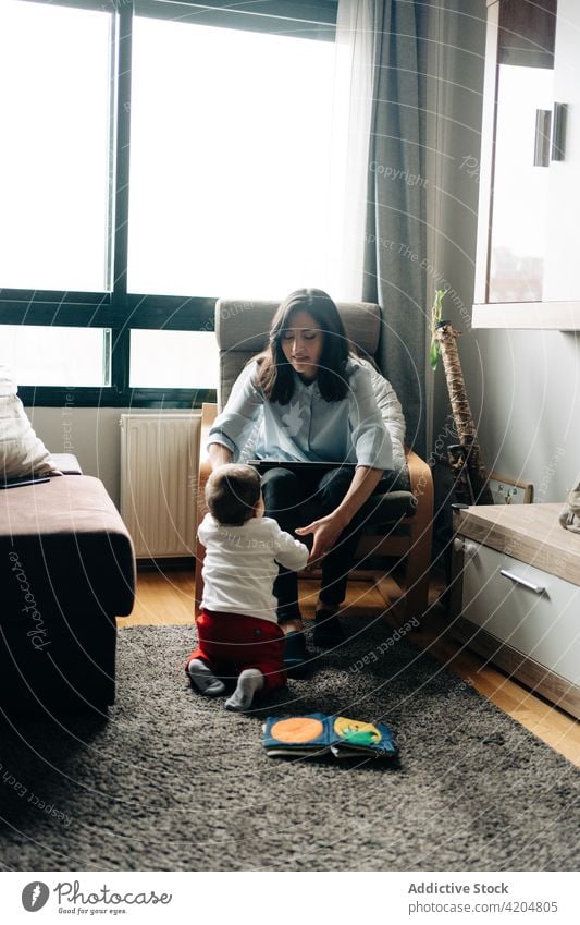 Mutter arbeitet am Laptop in der Nähe von lustigen kleinen Baby Sohn Arbeit Lächeln Stuhl freiberuflich Browsen zu Hause Elternschaft niedlich Frau Junge Kind