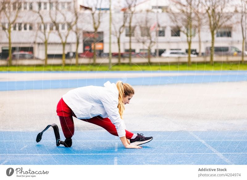 Entschlossene Sportlerin mit Beinprothese beim Stretching im Stadion Prothesen Dehnung Läufer Training professionell Athlet Frau paralympisch Aufwärmen passen