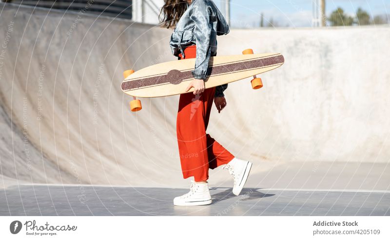 Aufgeregte Frau mit Longboard springt gegen blattlose Bäume in der Stadt stylisch Athlet trendy Spaziergang Stil genießen cool Individualität Schnüffler