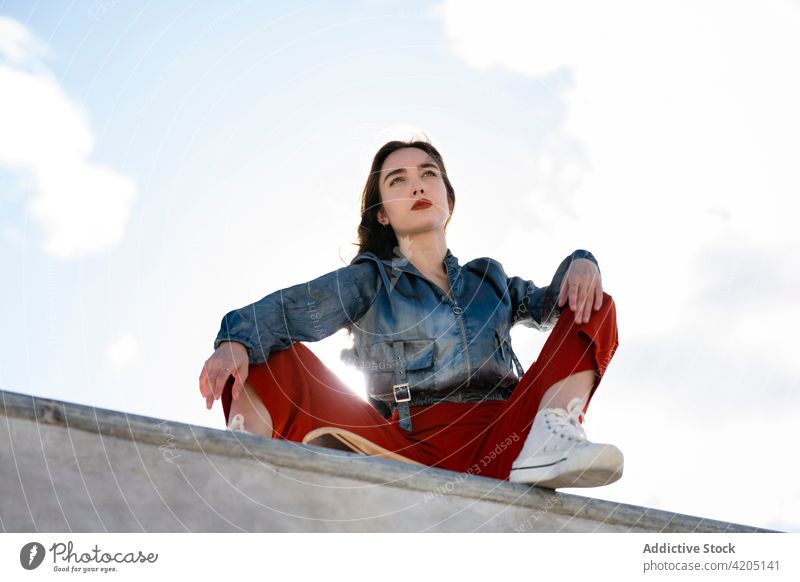 Stylischer Teenager unter blauem, bewölktem Himmel in der Stadt Mode Stil selbstbewusst Individualität cool tausendjährig Blauer Himmel wolkig Zaun ruhen