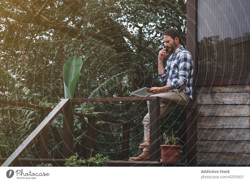 Nachdenklicher männlicher Architekt, der in der Nähe seines Hauses mit seinem Smartphone spricht Mann sprechen diskutieren Projekt Papier Schriftstück Terrasse