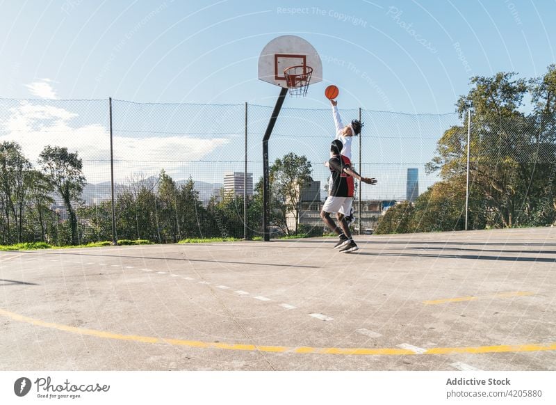 Schwarzer Mann und hispanischer Freund spielen Streetball auf einem Sportplatz Spieler Zusammensein Männer Basketball Reifen punkten multiethnisch Spielplatz