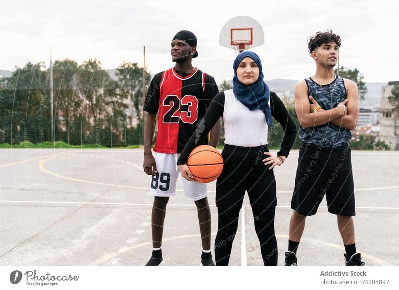 Unterschiedliche Streetball-Spieler stehen gemeinsam auf dem Basketballplatz Team Sportpark Zusammensein Bestimmen Sie Ball Straße Gericht multiethnisch