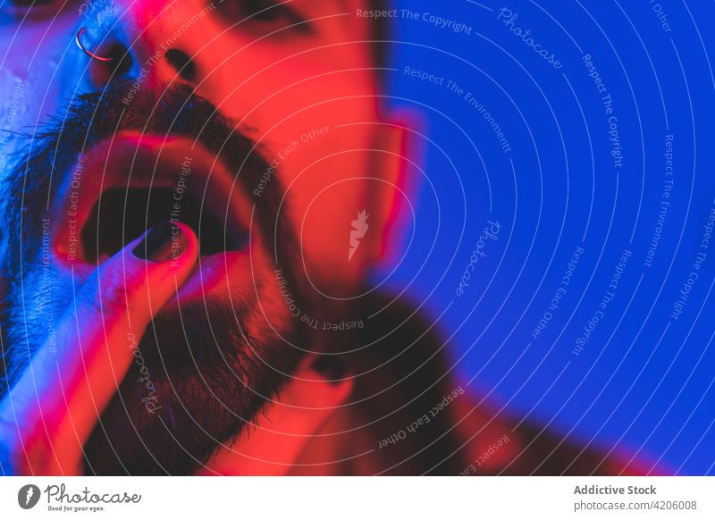 Hipster-Mann berührt Lippen in Neon-Beleuchtung Vollbart extravagant alternativ neonfarbig Lippen berühren exzentrisch informell Stil Mund nageln Piercing