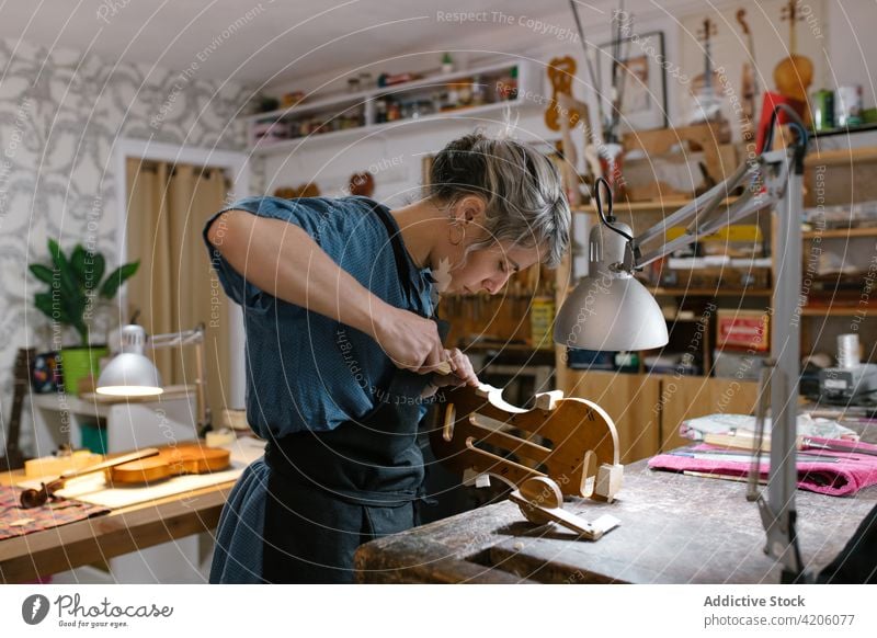 Handwerkerin beim Geigenbau in der Werkstatt schnitzen professionell Inszenierung Kurve Instrument Hobelbank Frau Kunstgewerbler Schürze Körper Lampe Arbeit