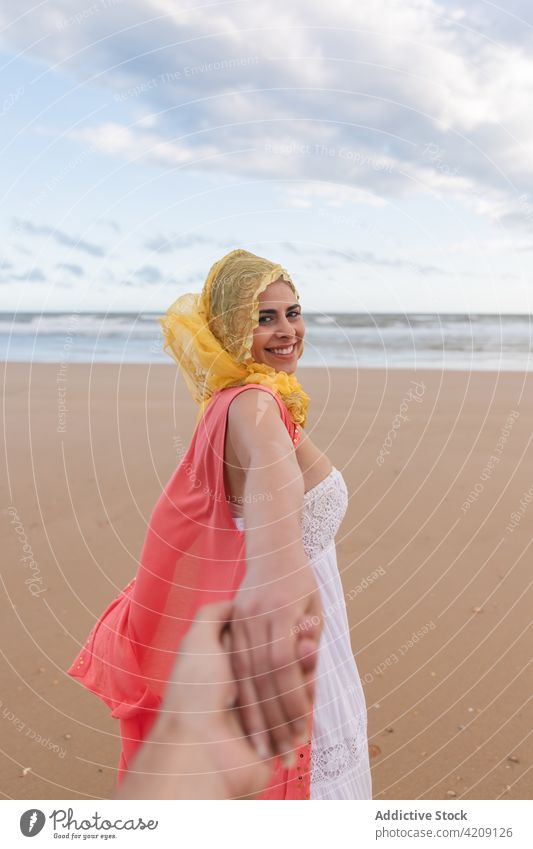 Fröhliche junge Frau, die ihrem Freund am Sandstrand die Hand reicht mir folgen Strand froh Lächeln heiter Händchenhalten Liebe romantisch Glück Zusammensein