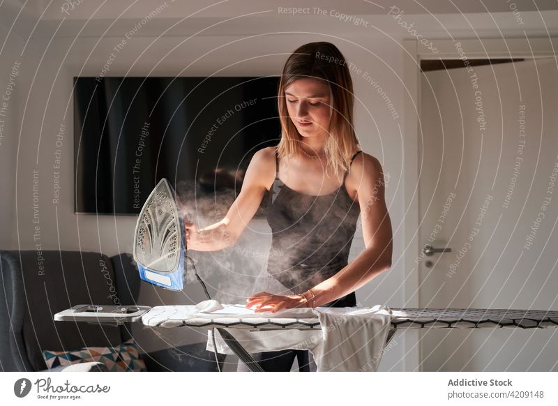 Konzentrierte Frau beim Bügeln von Kleidung zu Hause bügeln Stoff heimwärts Wochenende Bügelbrett ernst jung Hausarbeit Konzentration Fokus sonnig lässig