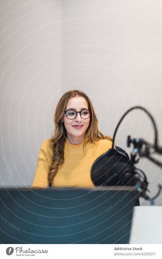 Fröhliche Frau arbeitet am Laptop im Radiosender Arbeit Ausstrahlung Atelier Mikrofon Gerät Browsen Surfen speziell modern Netbook Tisch positiv professionell