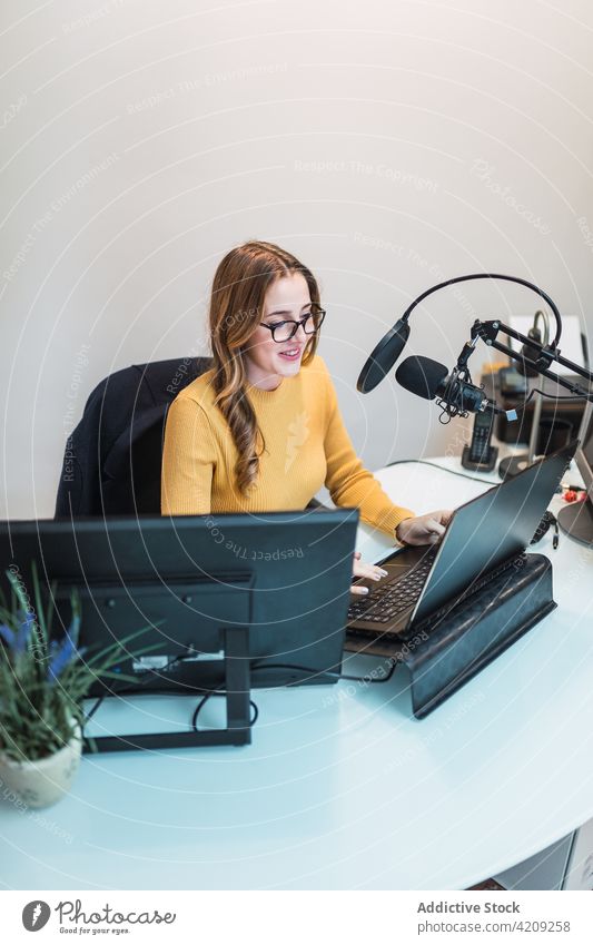 Fröhliche Frau arbeitet am Laptop im Radiosender Arbeit Ausstrahlung Atelier Mikrofon Gerät Browsen Surfen speziell modern Netbook Tisch positiv professionell