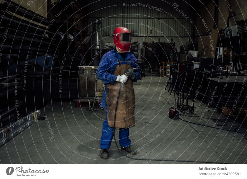 Unbekannter Schweißer mit Schutzhelm und Schweißschlauch in der Garage Person Mechaniker Handwerker Werkstatt Arbeiter Spezialist Gerät Uniform Konstruktion