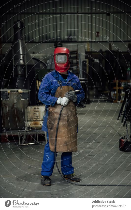 Unbekannter Schweißer mit Schutzhelm und Schweißschlauch in der Garage Person Mechaniker Handwerker Werkstatt Arbeiter Spezialist Gerät Uniform Konstruktion