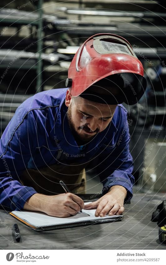 Konzentrierter Mechaniker in der Werkstatt, der Notizen in einen Notizblock schreibt Mann zur Kenntnis nehmen Notebook Konzentration Arbeiter Garage Spezialist