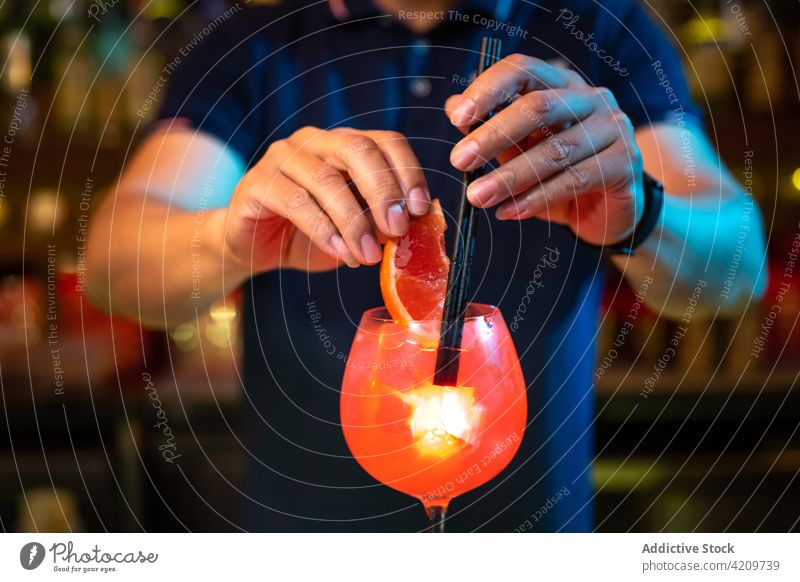 Junger Barkeeper beim Dekorieren eines Cocktails mit Grapefruitkeilen und Strohhalmen in der Bar Alkohol alkoholisch Aperitif Barista Barmann Getränk Business