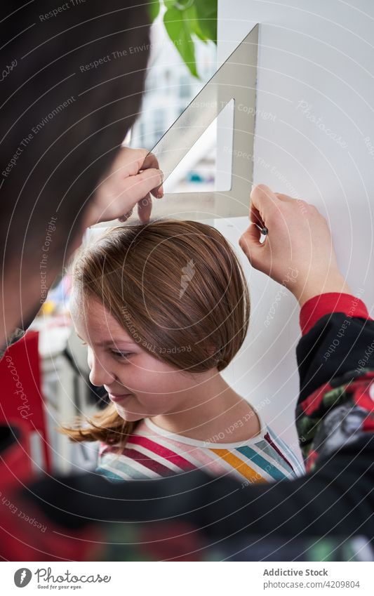 Crop-Eltern messen die Höhe des Kindes an der Wand Mädchen Lineal wachsen Lächeln Mark heimwärts niedlich Zusammensein Elternschaft positiv Freude Glück heiter