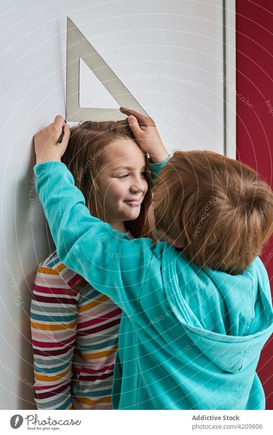 Kinder haben Spaß und messen die Höhe an der Wand Lineal Mark Zusammensein Spaß haben wachsen Geschwisterkind sorgenfrei Lächeln heimwärts niedlich Schwester