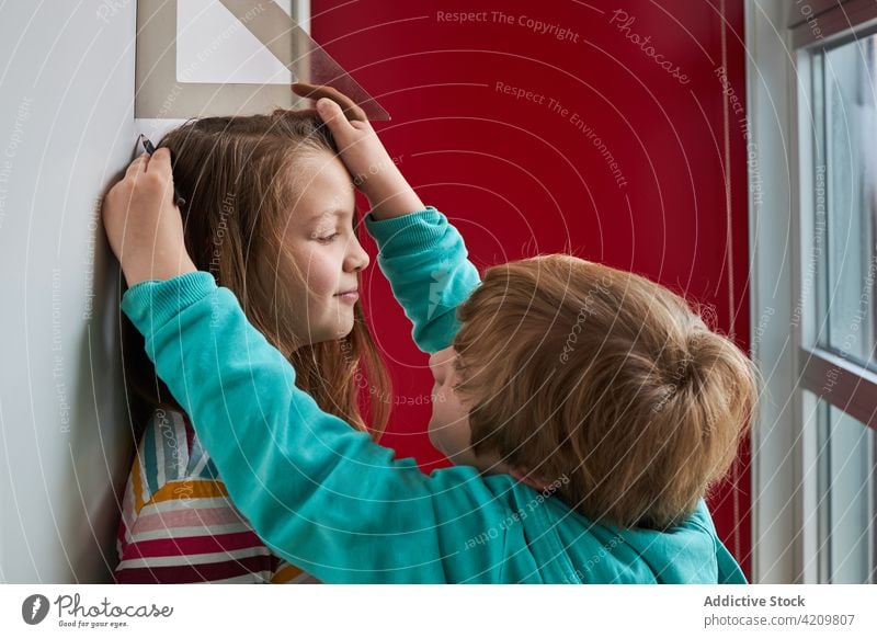 Kinder haben Spaß und messen die Höhe an der Wand Lineal Mark Zusammensein Spaß haben wachsen Geschwisterkind sorgenfrei Lächeln heimwärts niedlich Schwester