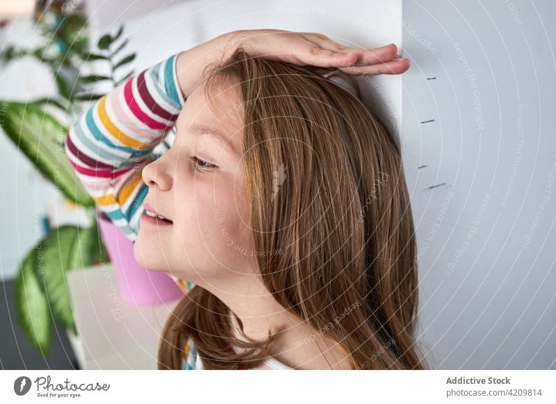 Lächelndes Mädchen, das seine Körpergröße in der Nähe der Wand zu Hause misst messen Höhe heimwärts wachsen niedlich Kind Mark positiv Freude Glück heiter