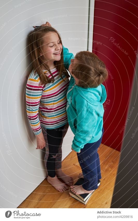 Fröhliche Kinder messen zu Hause die Höhe an der Wand Mark Geschwisterkind Zusammensein Spaß haben wachsen sorgenfrei Lächeln heimwärts niedlich Schwester