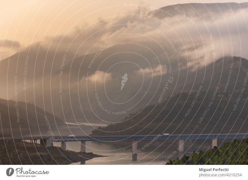 Kühltransporter auf einer Brücke über einen Sumpf, umgeben von Bergen und Wäldern mit niedrigen Wolken bei Sonnenaufgang. Sumpfgebiet Landschaft Natur Wasser