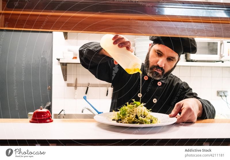 Männlicher Koch gibt Soße auf ein Gericht Mann Küchenchef Restaurant Speise Saucen hinzufügen eingießen Lebensmittel männlich appetitlich Beruf Job Mahlzeit