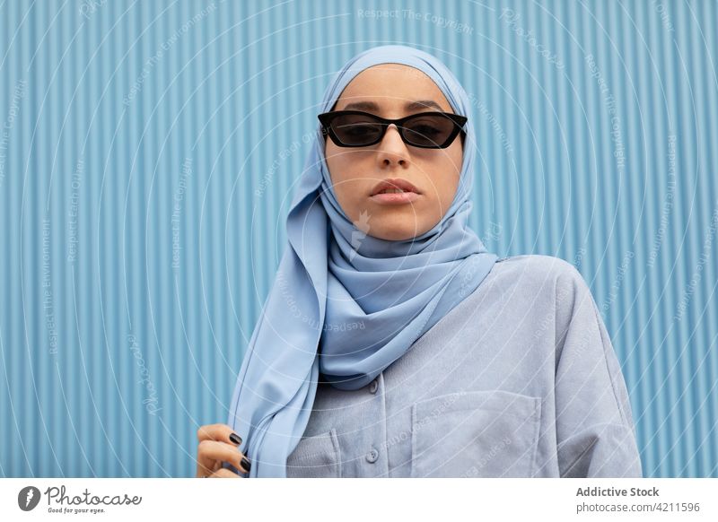 Trendige muslimische Frau mit Sonnenbrille auf blauem Hintergrund Mode Stil Kopftuch nachdenken Individualität Accessoire Islam Porträt lässig cool modern Farbe