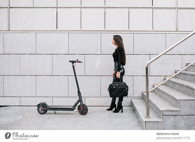 Stilvolle Geschäftsfrau steht in der Nähe von Elektro-Roller in der Stadt elektrisch Tretroller Verkehr Großstadt Straße Unternehmer modern urban Frau Schritt