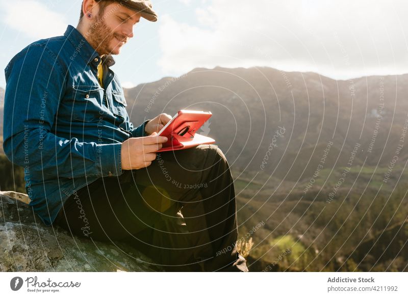 Reisender mit Tablet auf einem felsigen Hügel im Hochland sitzend Berge u. Gebirge Mann bewundern genießen Aussichtspunkt Tablette Freiheit reisen männlich