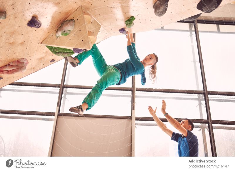 Sportlerin an der Kletterwand im Bouldering Center Aufstieg Wand Felsbrocken Training Gleichgewicht stark Ausbilderin Überwachung extrem Trainerin Bergsteiger