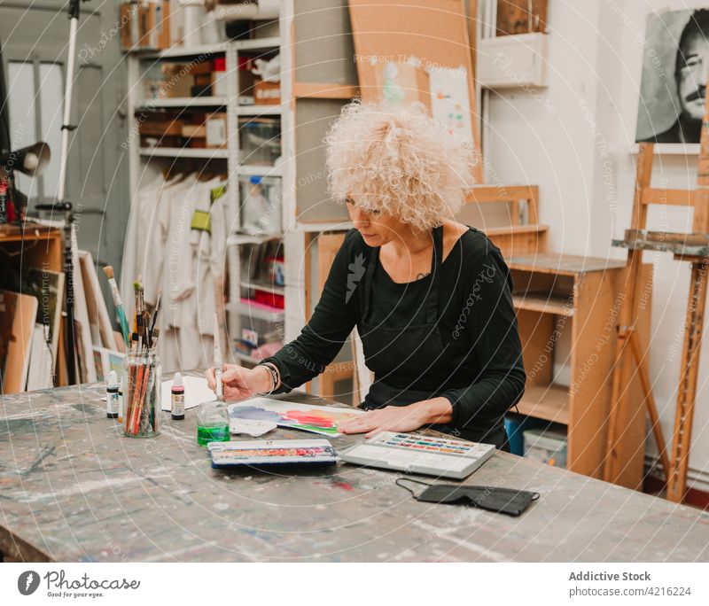 Ernste Frau malt auf Papier im Kunstatelier Künstler Farbe Anstreicher Wasserfarbe Pinselblume Werkstatt Handwerkerin kreativ Atelier Fokus ernst Talent