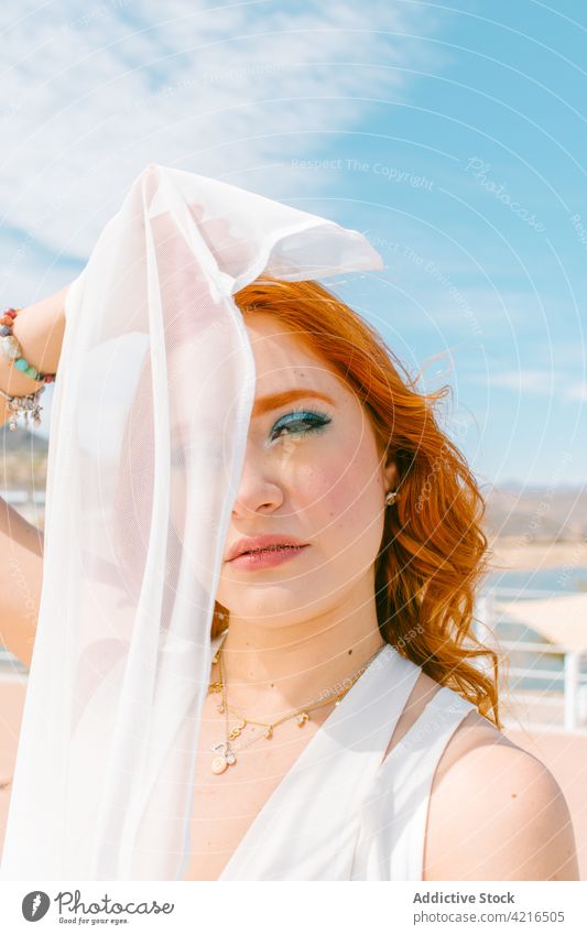 Braut mit Make-up unter blauem bewölktem Himmel im Sonnenlicht Auge abdecken Imkerschleier Hochzeit feiern feminin sanft romantisch festlich Porträt Frau wolkig