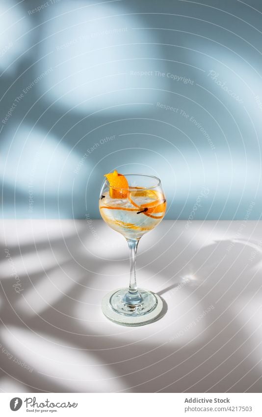 Glas Gin Tonic mit Orangenzesten auf dem Tisch Cocktail Alkohol hochball orange Schale Gewürznelke Schatten Wittern hell kreativ Design Wasser Aroma