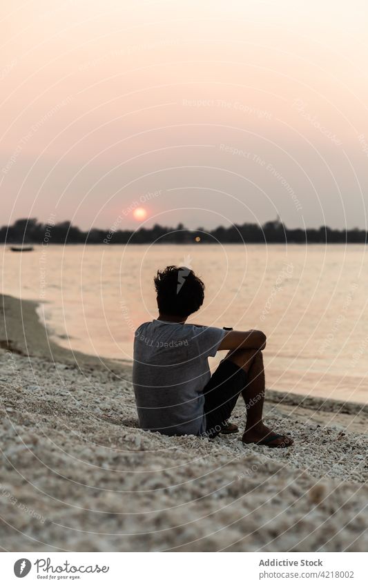 Anonymer Mann, der sich in der Dämmerung an der sandigen Küste ausruht Meeresufer Sonnenuntergang bewundern Strand genießen friedlich Seeküste Strandpromenade