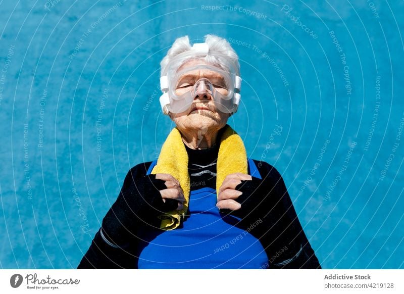 Ältere Frau mit Kopfbedeckung beim Boxen und Handtuch auf der Schulter Sportlerin Boxsport Senior Schutzhelm ernst sportlich aktiv Beschützer Energie reif