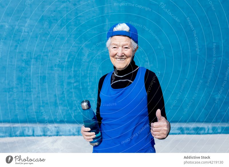 Fröhliche ältere Sportlerin mit Wasserflasche im Outdoor-Sportzentrum Zahnfarbenes Lächeln Flasche Sportkleidung Vitalität aktiv Fitness reif Motivation Energie