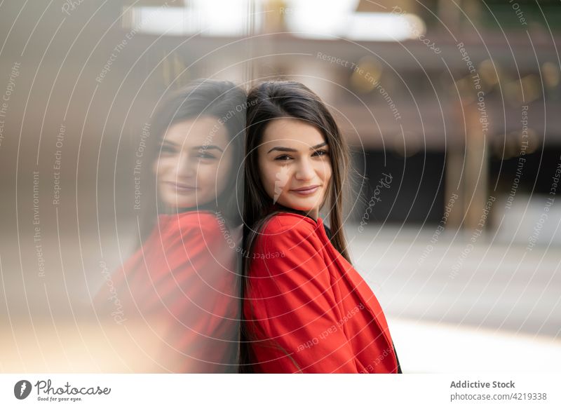 Fröhliche Frau in roter Kleidung in der Stadt stehend Jacke Outfit Lächeln charmant Großstadt urban fettarm Wand heiter Straße positiv Freude modern lässig