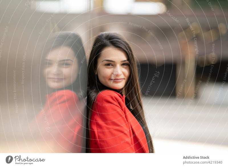 Fröhliche Frau in roter Kleidung in der Stadt stehend Jacke Outfit Lächeln charmant Großstadt urban fettarm Wand heiter Straße positiv Freude modern lässig