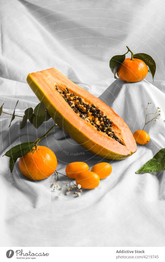 Papaya zwischen Mandarinen und Kumquats auf geknittertem Stoff schneiden Frucht tropisch natürlich frisch Vitamin Blatt Gewebe geschnitten Hälfte Samen reif