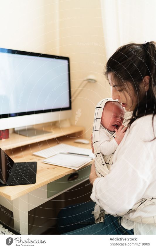 Mutter, die ihr neugeborenes Baby am Schreibtisch im Haus kuschelt kuscheln Säuglingsalter Mutterschaft Liebe unschuldig Angebot heimwärts Frau Mama Träger