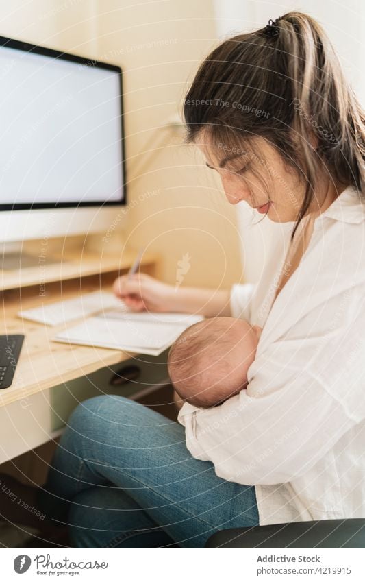 Mutter, die ihr Baby stillt und in einem Haus in ein Heft schreibt Frau stillen freiberuflich Schönschreibheft Mutterschaft Säuglingsalter neugeboren heimwärts