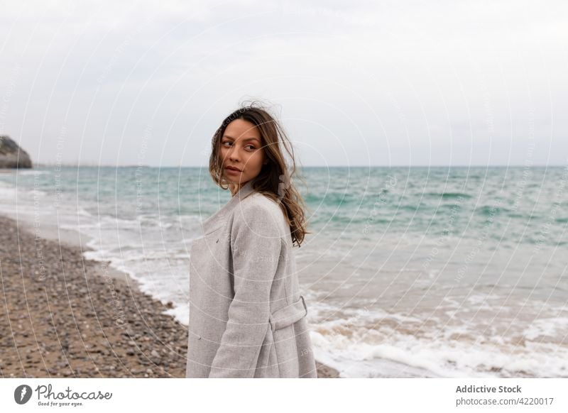 Ruhige Frau, die an einem bewölkten Tag am sandigen Meeresufer steht Strand Herbst wolkig Sand ruhig charmant Mantel Windstille Ufer stehen Harmonie Frieden