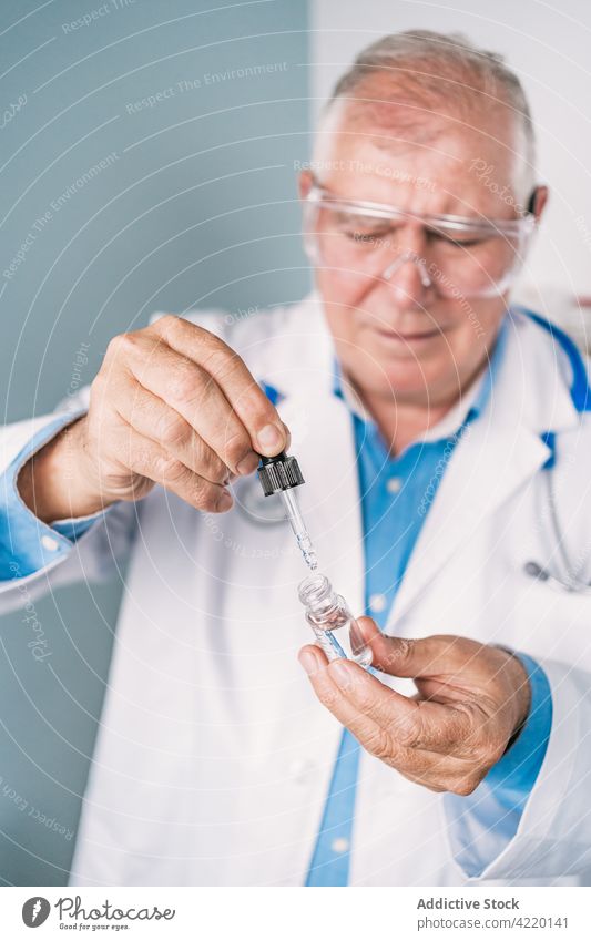 Oberarzt mit Pipette und Tropfenflasche in der Klinik Dosis medizinisch Erdöl liquide professionell Mann Tropfer schützend Brille Uniform durchsichtig Flasche