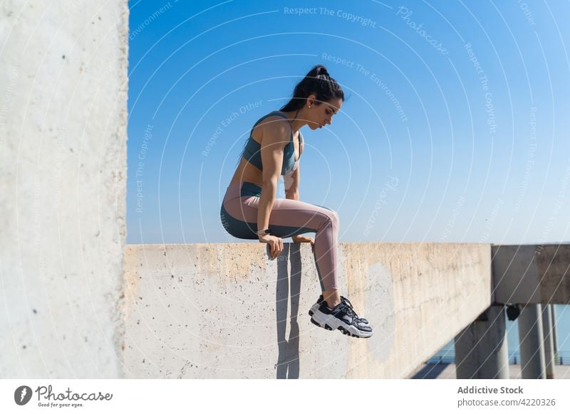 Sportlerin auf Betonzaun nach Training im Freien muskulös sportlich Körper stark Wellness Gesunder Lebensstil Sportkleidung Zaun Blauer Himmel Frau Pause Kurve