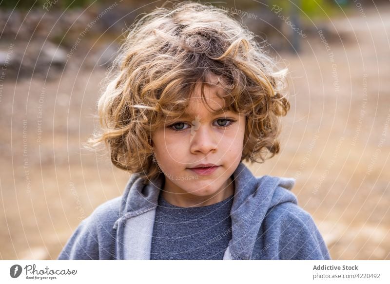 Junge im Kapuzenpulli mit gewellten Haaren bei Tageslicht charmant freundlich Kindheit herzlich wehmütig lässig Stil allein Porträt grau weich anhaben